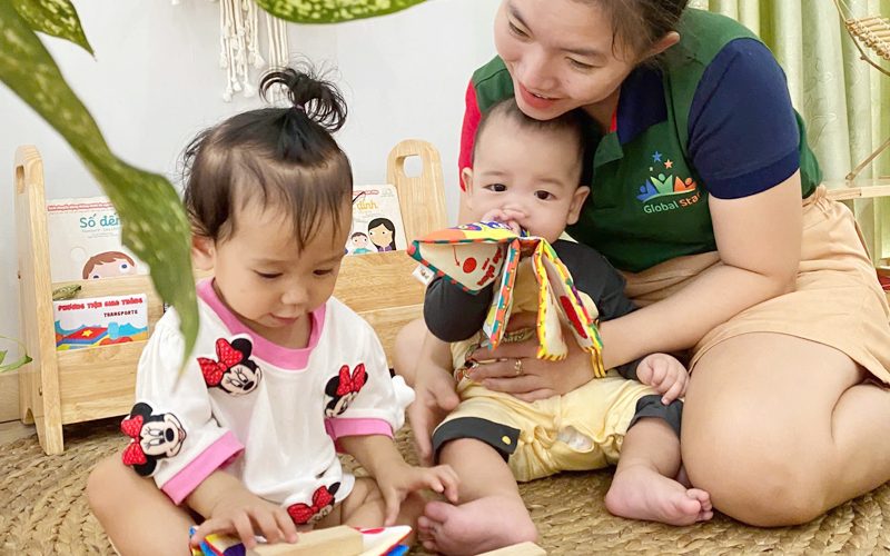 Cô ngồi trên thảm chơi cùng hai bé nhỏ