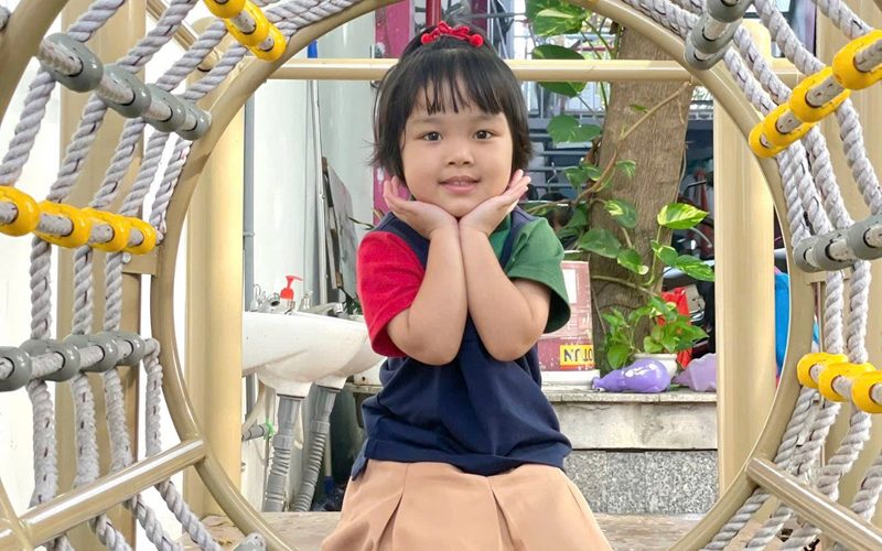 Bé gái mặc đồng phục ngồi cười trong khu leo trèo
