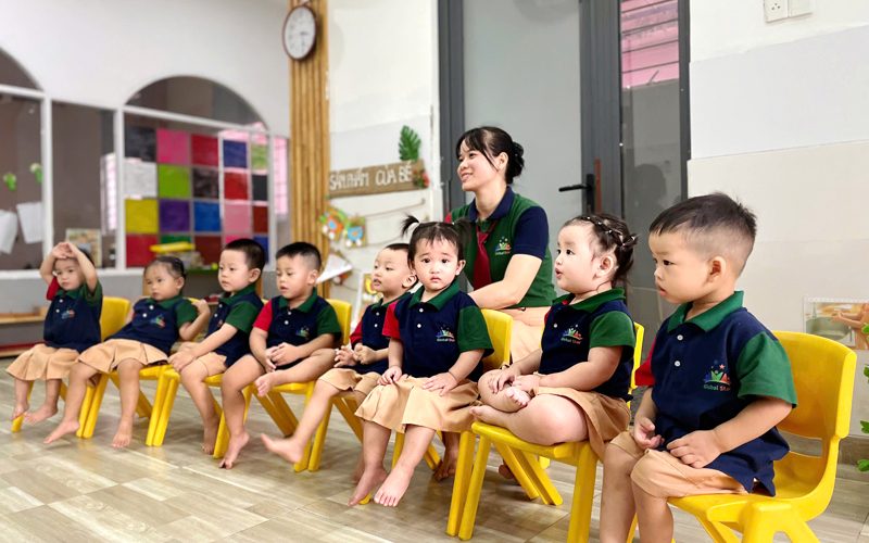 Các bé mặc đồng phục ngồi ghế vàng thành hàng trong lớp học sáng sủa của Global Star School